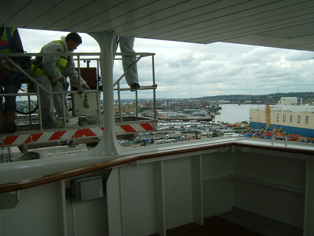 Some workmen touching up the ship from a giant crane standing on the dock. This is ship's eleventh d...
