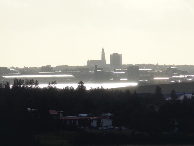 Reykjavik, with sunlight both behind it and reflecting off the water in front of it.