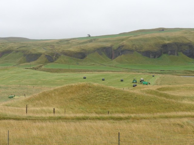 A farm, a cliff with grass-covered scree, and some big antennas on the hilltop.