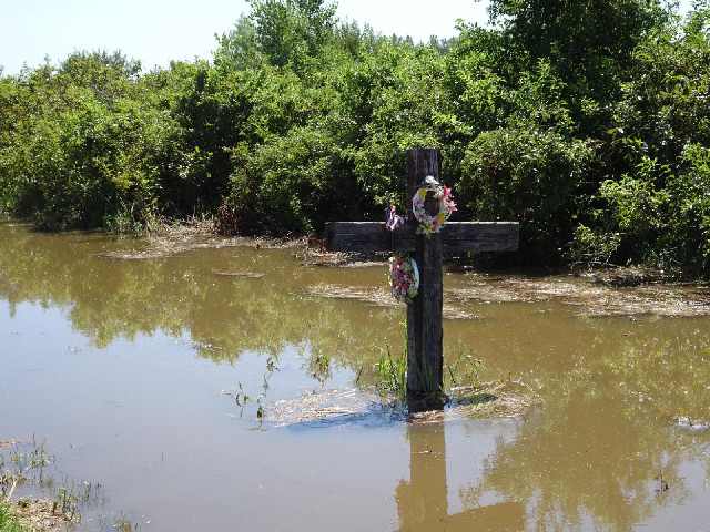 A cross in a flooded ditch next to the road.