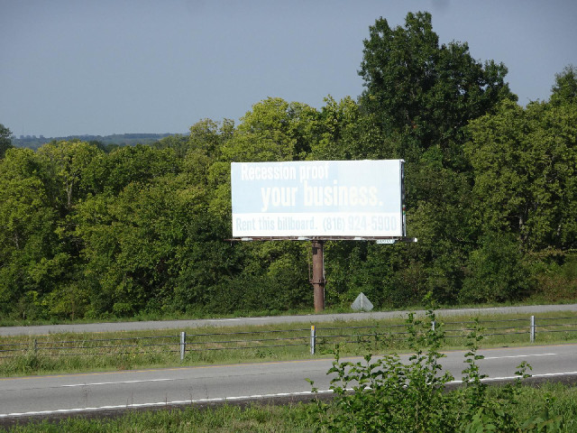 This severely faded sign says "Recession proof your business. Rent this billboard". That i...