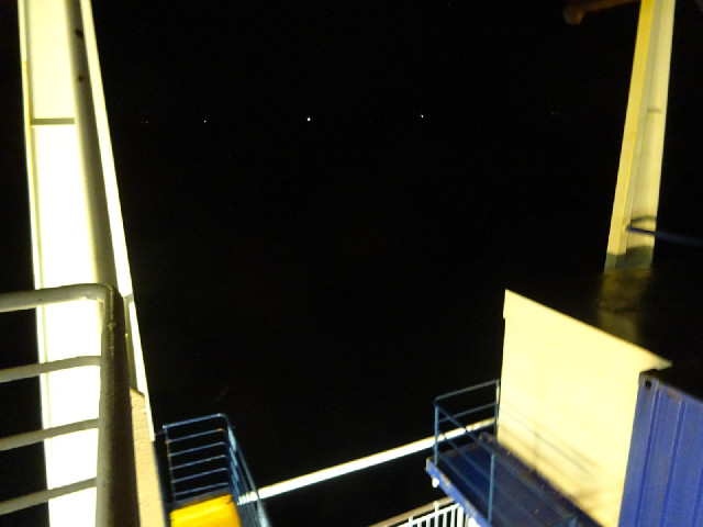The dots are lights on the Enlish coast. The feint smudge just above the corner of the blue handrail...