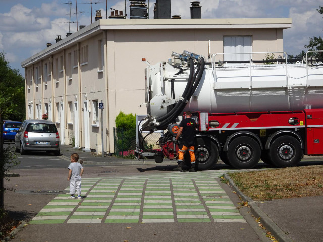 The man is about to clean out a drain in thre road. The little boy seems fascinated by it.