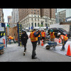 Workers controlling the flow of pedestrians through where they are shifting concrete.